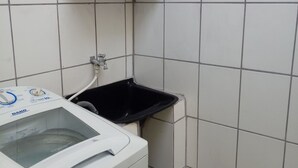 A compact laundry area with a front-loading washing machine, a small black sink, and a tiled wall. - Beachfront house in Bertioga, 50 meters or 2 minutes from Indaiá Beach. (Bertioga)