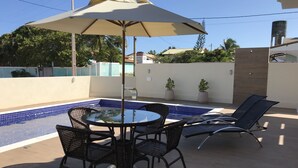 An outdoor pool area with a table and chairs, surrounded by a tiled deck. - Modern house in Barra do Jacuípe, 180m from the beach. (Camaçari)