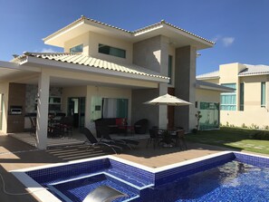Una moderna casa a due piani con piscina, area salotto esterna e patio.