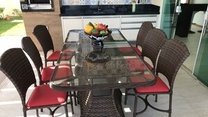 A glass-top dining table with wicker chairs, a kitchen in the background, and a potted plant on the counter. - Modern house in Barra do Jacuípe, 180m from the beach. (Camaçari)