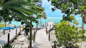 Una passerella in legno conduce a una spiaggia con acque cristalline turchesi e una vista lontana sull'oceano.