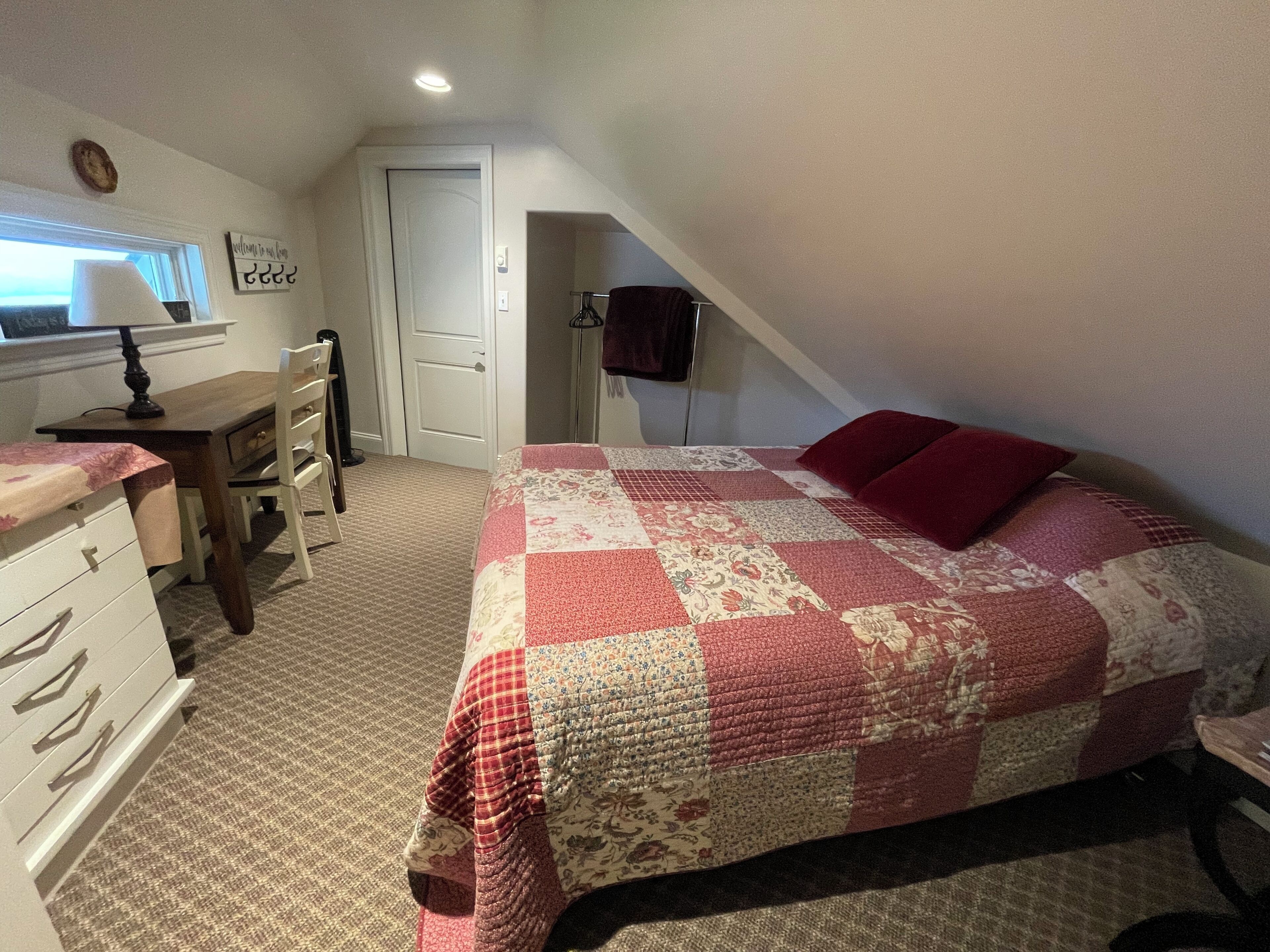 A bedroom with a bed, dresser, desk, and a door.
