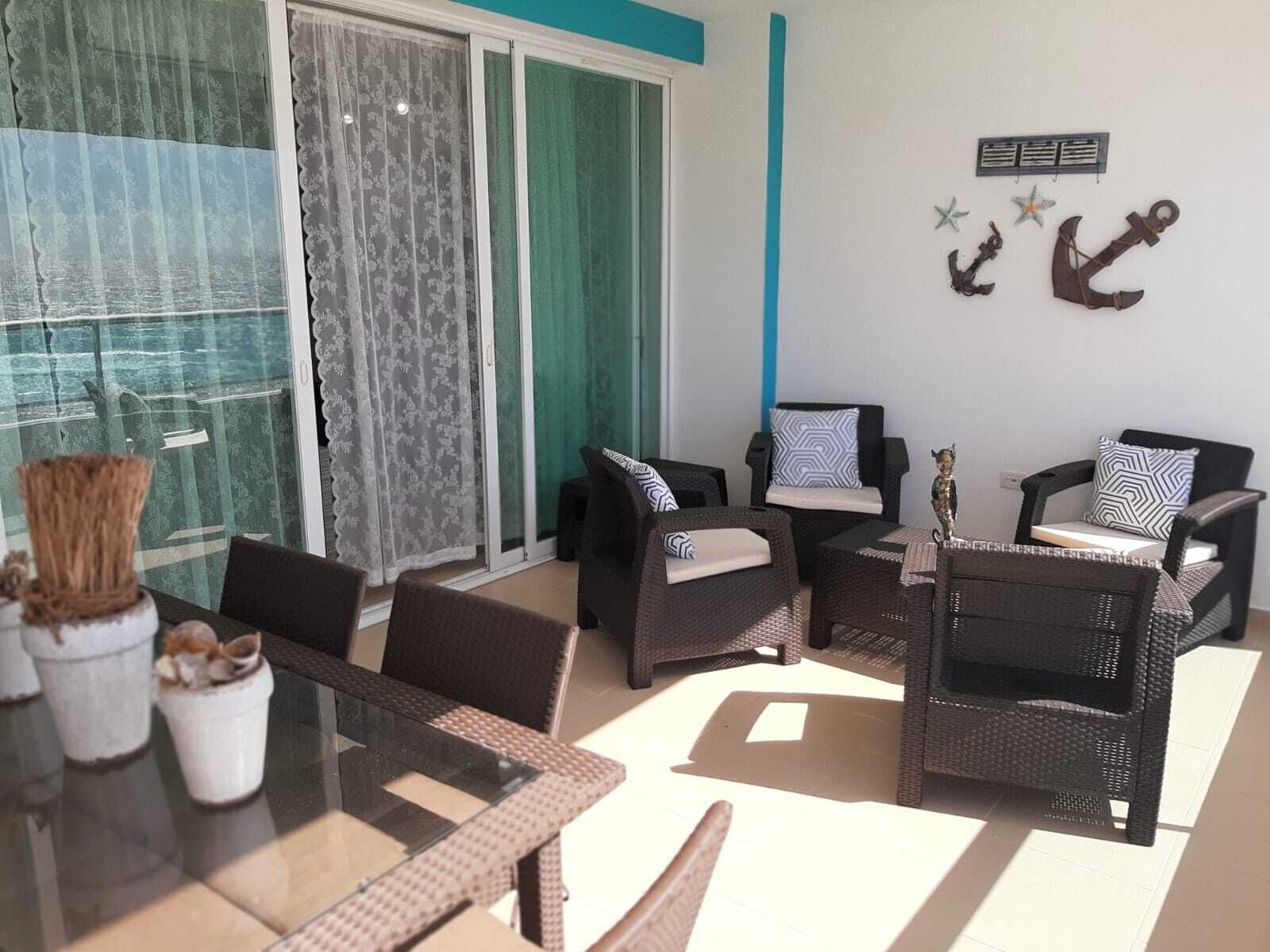 Un balcón amoblado con muebles de mimbre, una mesa de vidrio y adornos en la pared.