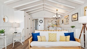 A cozy room with a wooden bench, a desk, and a white sofa with blue and yellow cushions. - Romantic Oceanfront Studio With Private Deck | Right On The Sand! (Santa Barbara)