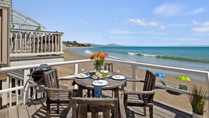 A wooden deck with a table set for two, overlooking a beach with waves and a clear sky. - Romantic Oceanfront Studio With Private Deck | Right On The Sand! (Santa Barbara)