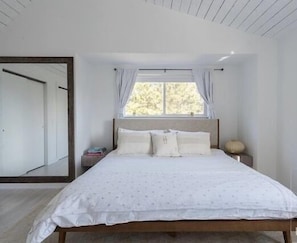A bedroom with a large bed, a window with curtains, a nightstand, and a mirror on the wall. - Ideal Montauk retreat with pool and hottub (Montauk)