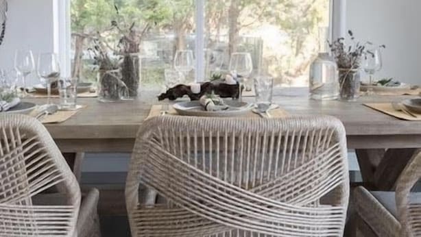Un coin repas avec une table en bois dressée pour quatre personnes, des chaises en osier et une grande fenêtre donnant sur la forêt.