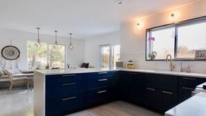 Une cuisine moderne avec des meubles bleu foncé, un grand îlot central doté d’un plan de travail blanc et un éclairage suspendu.