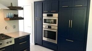 Une cuisine moderne avec des meubles de couleur sombre, des appareils en acier inoxydable et un plan de travail de couleur claire.