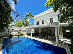Une maison moderne dotée d’une piscine, d’un espace salon extérieur et d’un patio couvert.