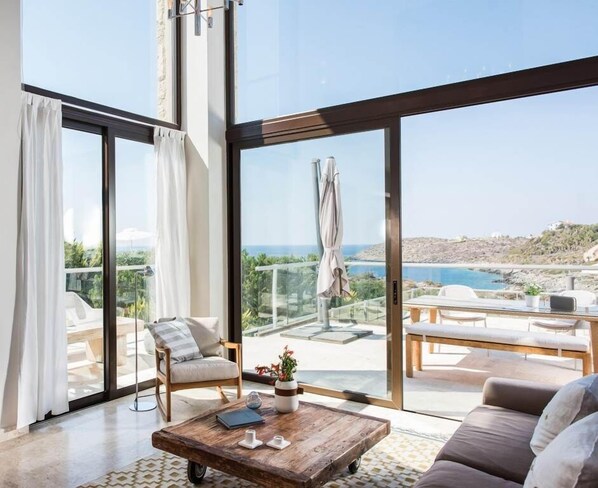 Relax in a spacious living room with a sofa, armchairs, and a coffee table, leading to a scenic outdoor terrace with a view of the coastline.