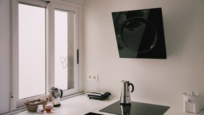 A kitchen with a coffee maker, kettle, juicer, and a small table with a notebook and a basket.