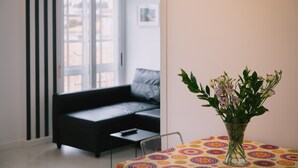 A living room with a black sofa, a small table with a vase of flowers, and a colorful tablecloth.