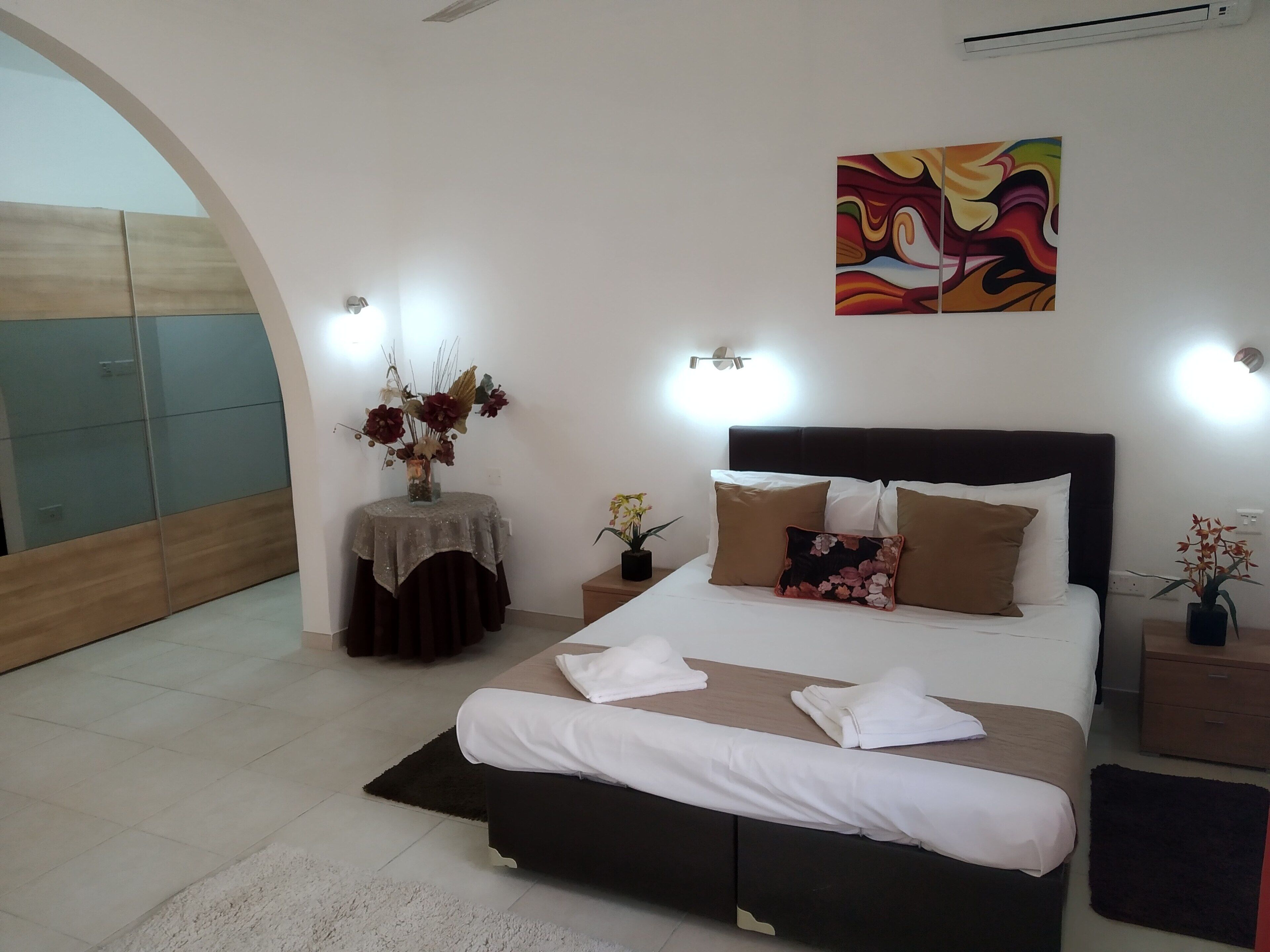 A modern bedroom with a large bed, a decorative vase, and a colorful abstract painting.