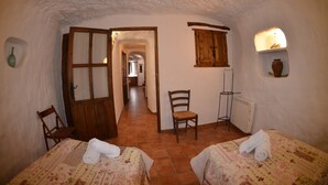 Una camera accogliente con due letti, una porta in legno, una sedia, un termosifone e una mensola con un vaso.
