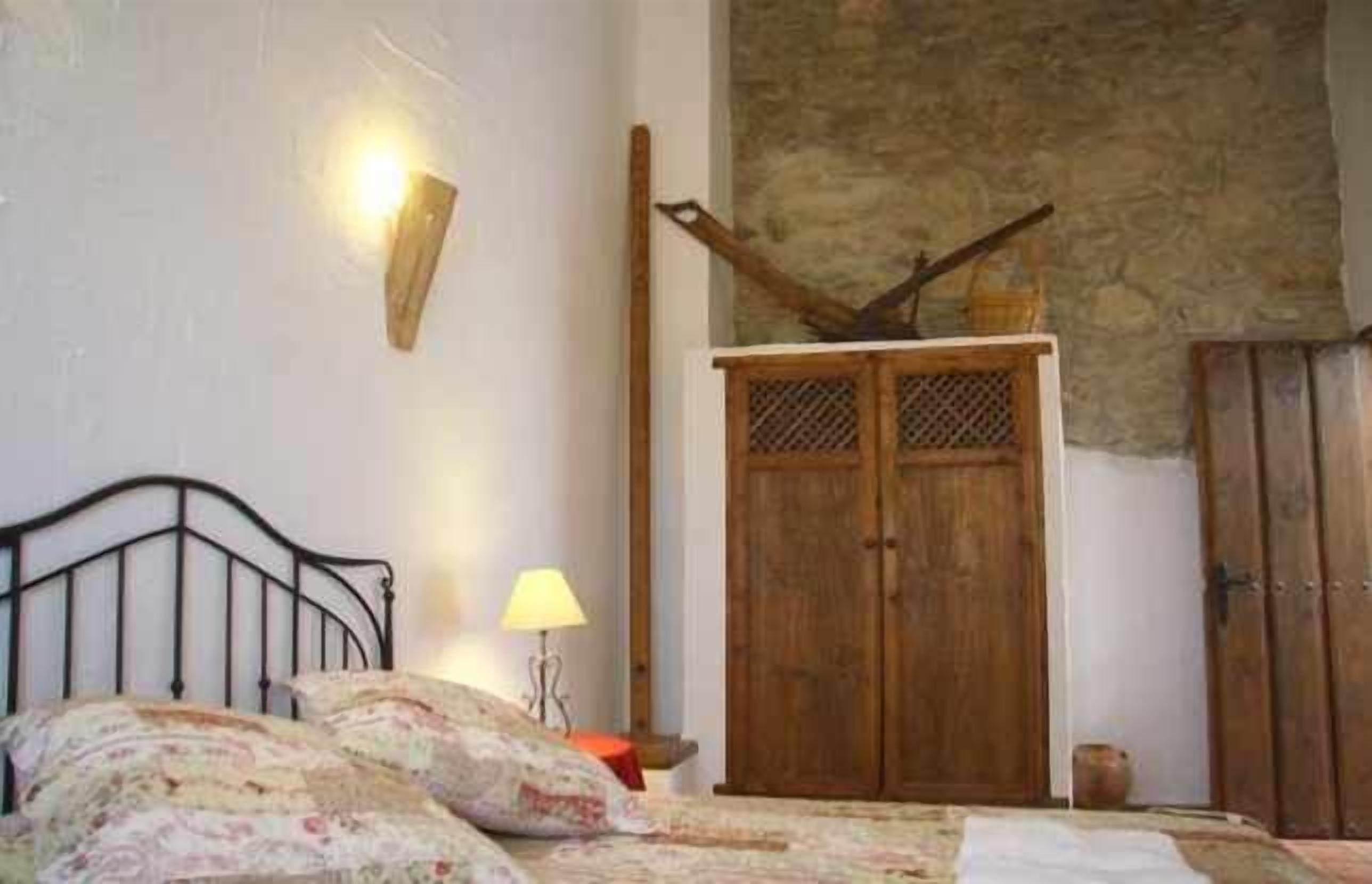 Un dormitorio con una cama, un armario de madera, una lámpara de pared y una pared de piedra.