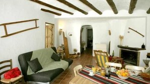Un soggiorno rustico con travi a vista in legno, un divano, un tavolo da pranzo con della frutta e un camino.