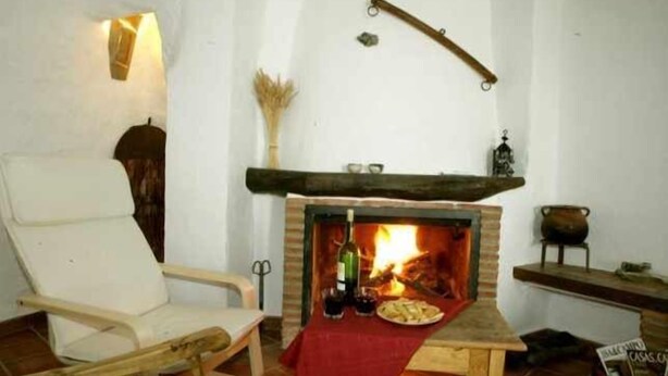 Una camera accogliente con camino, una sedia di legno e un tavolo con tovaglia rossa.