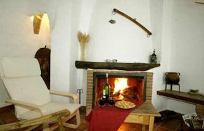 Ein gemütlicher Raum mit Kamin, einem Holzstuhl und einem Tisch mit roter Tischdecke.
