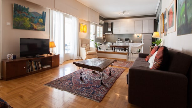 A spacious living room with a large TV, comfortable seating, and a kitchen in the background.