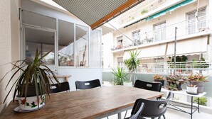 A wooden table with chairs, potted plants, and a view of a residential building with balconies.