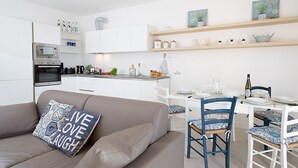 Een moderne keuken met witte kastjes, een ingebouwde oven en een eethoek met een witte tafel en blauwe stoelen.