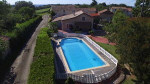 Une piscine rectangulaire entourée d’une clôture blanche, avec une terrasse dallée et une zone herbeuse.