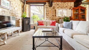 A living room with stone walls, a fireplace, a sofa, a coffee table, and a television. - House next door in Barcenaciones (Barcenaciones)