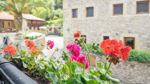 A stone building with multiple windows and a garden with red and pink flowers in front. - House next door in Barcenaciones (Barcenaciones)