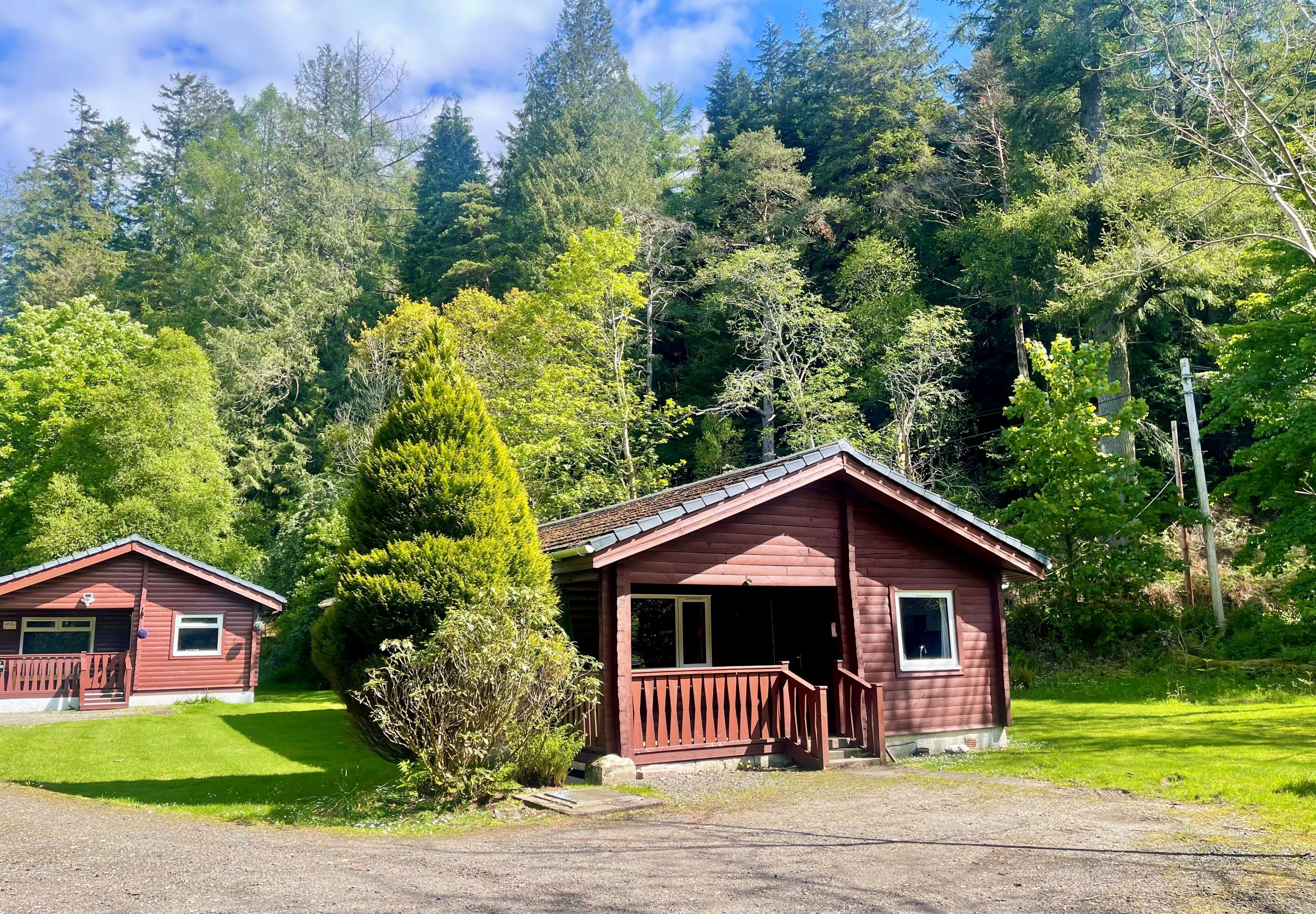 A cabin with a porch and a small deck, surrounded by dense forest.