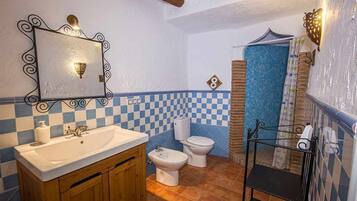 A bathroom with a checkered blue and white tile wall, a wooden vanity with a sink, a bidet, and a toilet.