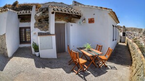 A traditional white building with a tiled roof, a wooden table with chairs, and a potted plant.