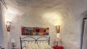 A bedroom with a bed, two bedside tables, a chair, and a wall with a colorful tapestry.