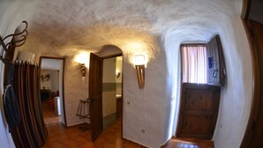 A narrow hallway with a wooden door, a light fixture, and a view into another room.