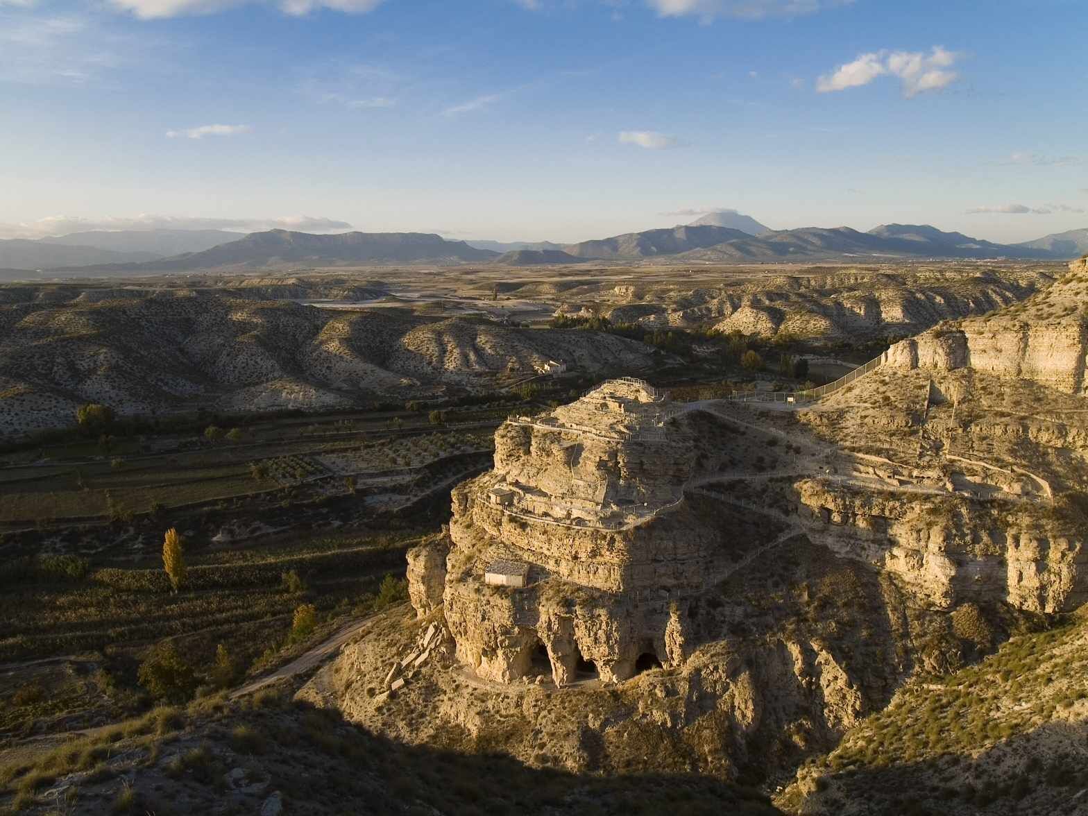 A rugged landscape with a prominent rock formation and terraced structures.