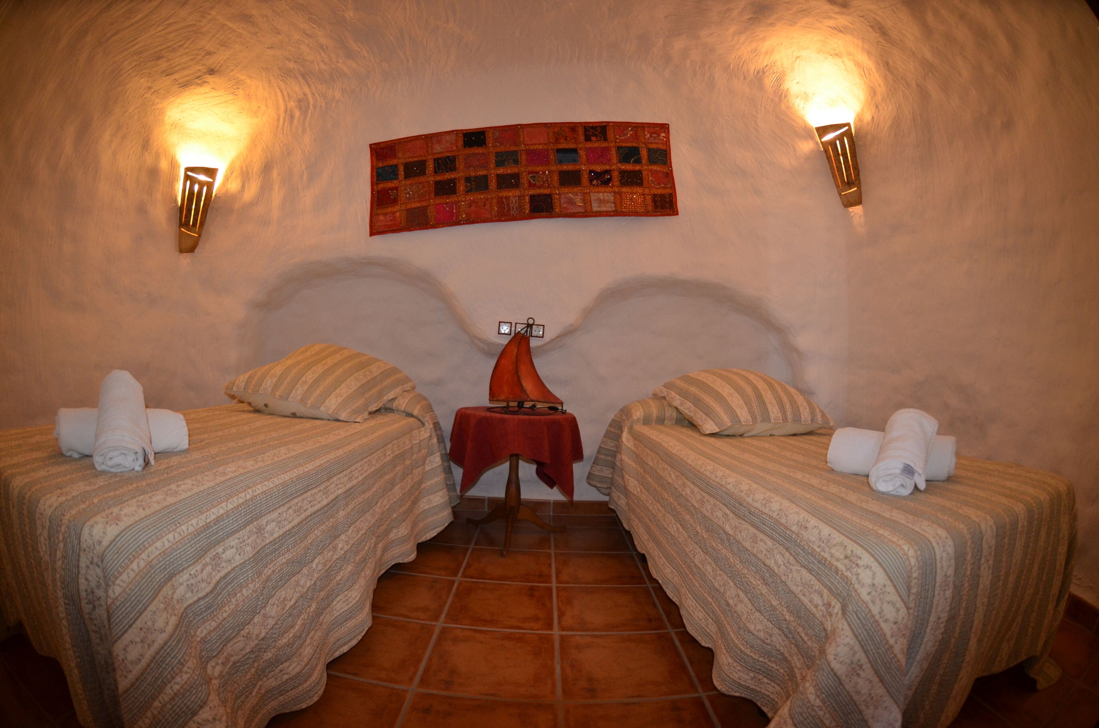 Una habitación acogedora con dos camas, una mesa roja y un tapiz acolchado en la pared.