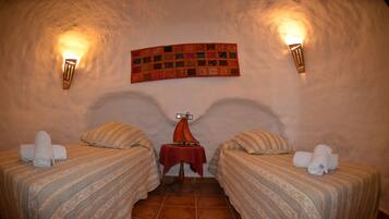 Una habitación acogedora con dos camas, una mesa roja y un tapiz acolchado en la pared.
