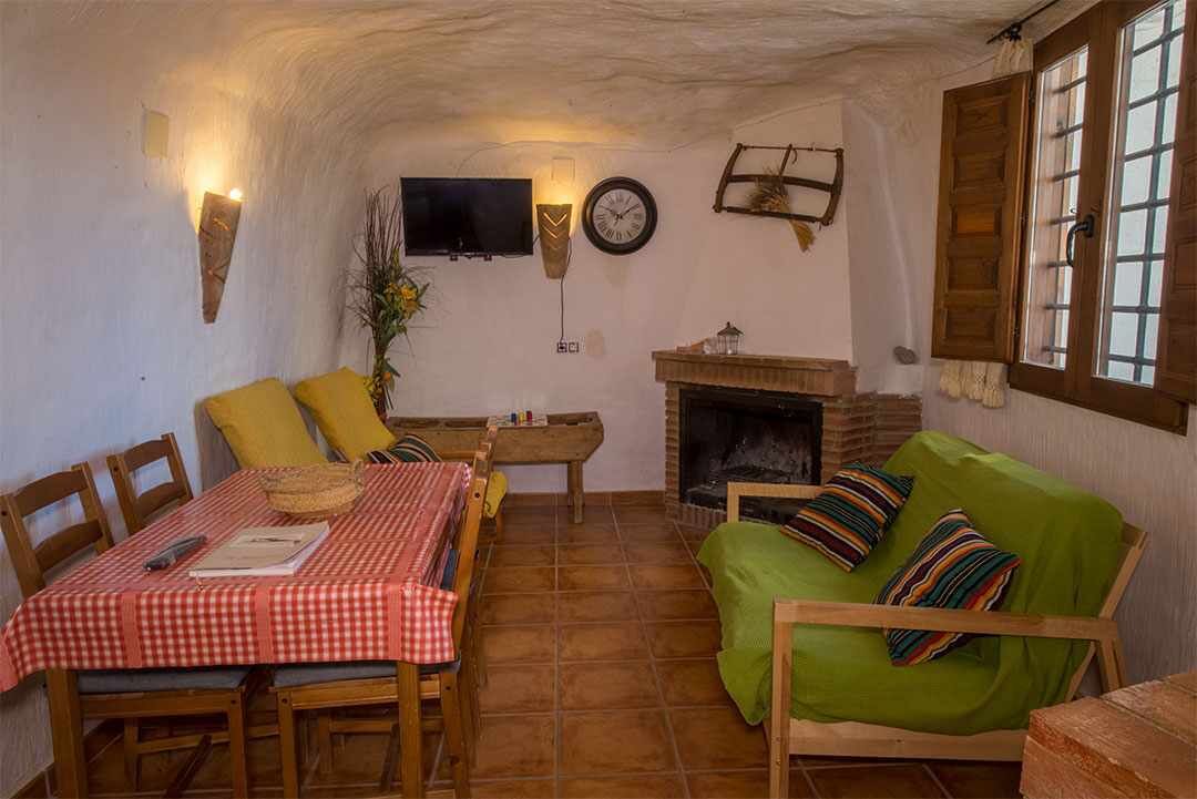 Een gezellige woonkamer met een open haard, een eettafel met geruit tafelkleed en een groene bank met gestreepte kussens.