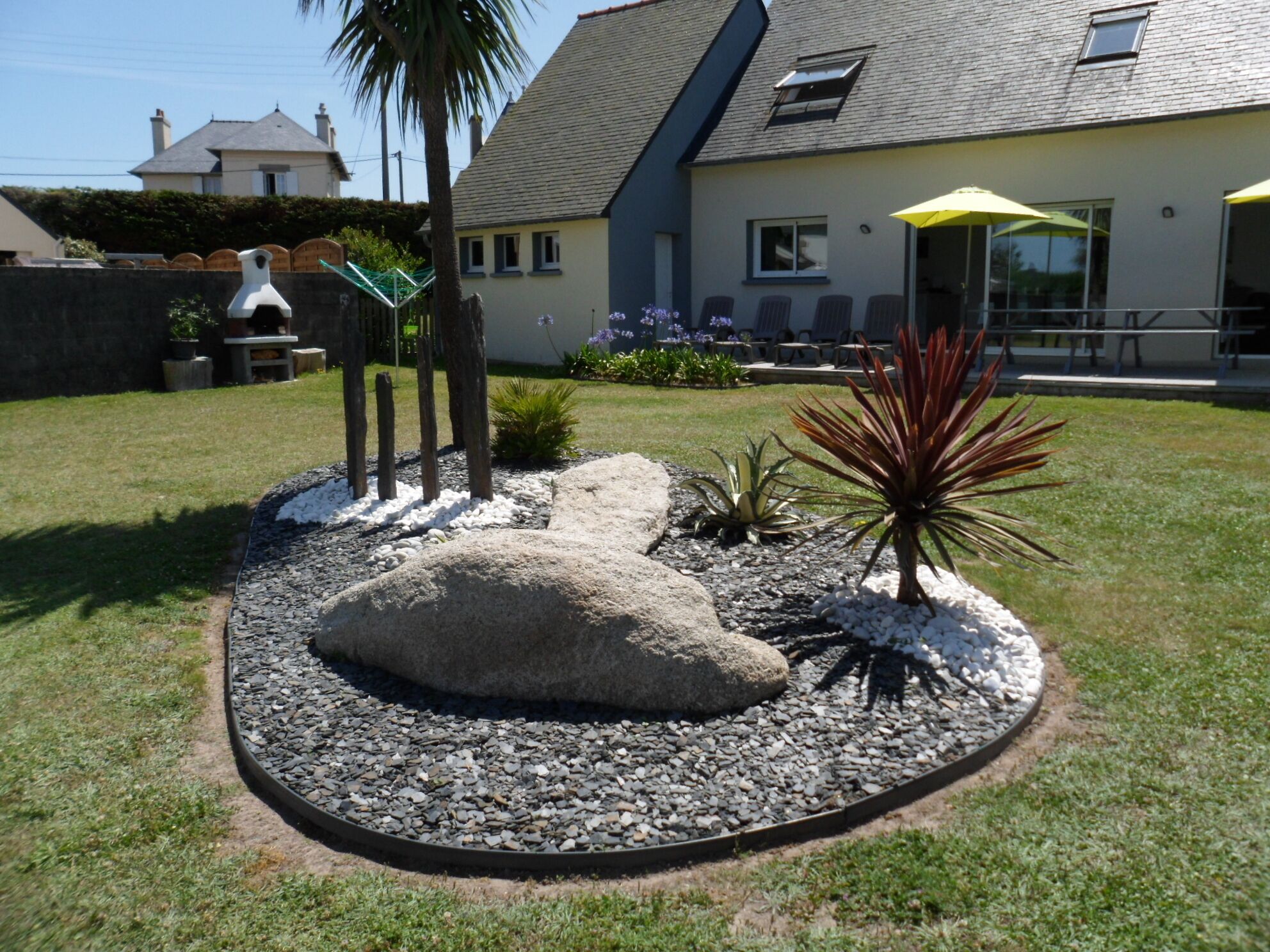 Un jardin aménagé avec une grande roche servant d’élément central, entouré de gravier et de différentes plantes.