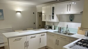 A modern kitchen with white cabinetry, a central island, a built-in oven, and a clock on the wall.