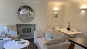 A modern living room with a sofa, a round table, a fireplace, and a dining area.