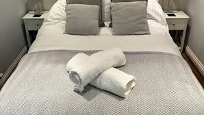 A neatly made bed with a patterned bedspread, two pillows, and a rolled towel. There are two bedside tables with lamps and a framed picture on the wall above the bed.