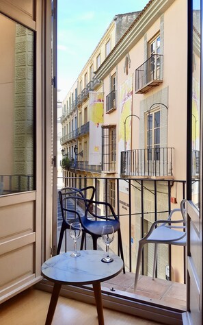 Ein Balkon mit zwei Tischen, jeder Tisch mit einem Weinglas, mit Blick auf ein Gebäude mit Balkonen und einem Schild, auf dem 'Museo Del Vino Malaga' steht.