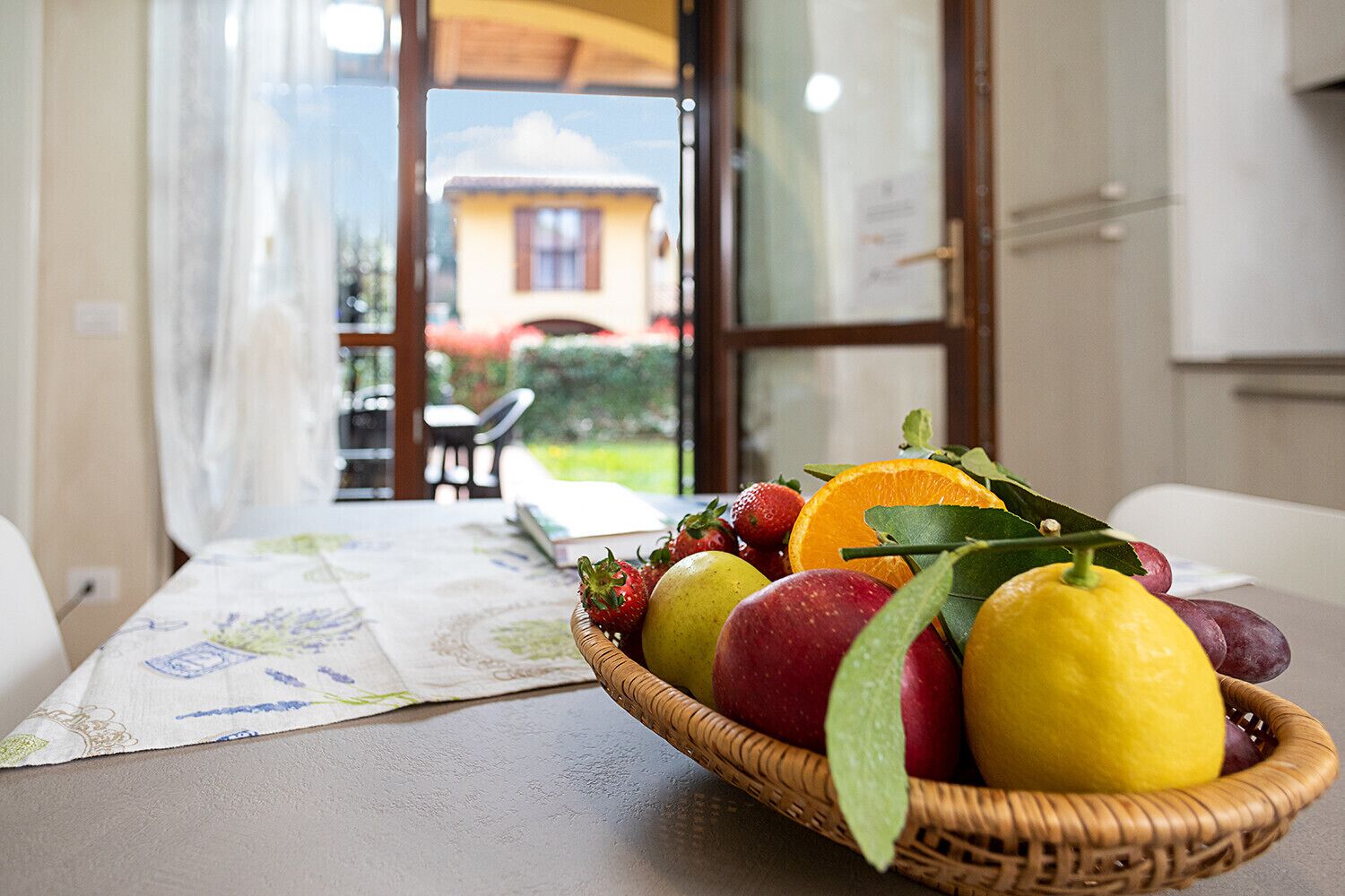 A dining table with a fruit basket containing strawberries, apples, and oranges.
