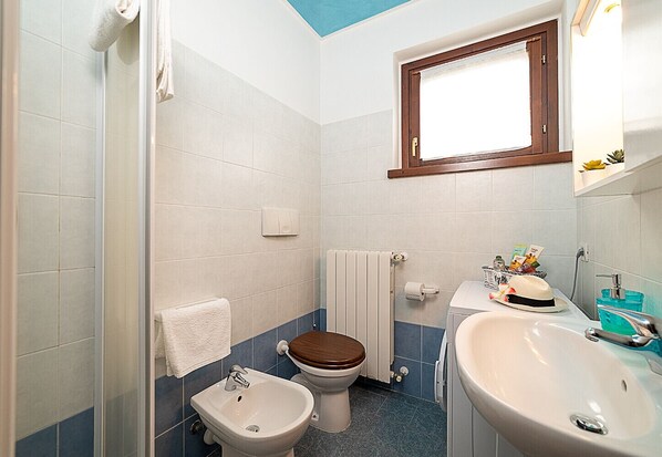 A bathroom with a bidet, toilet, sink, and a window with a wooden frame.