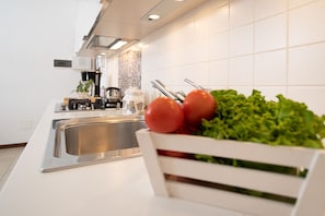 A modern kitchen with a stainless steel sink, a white countertop, and a bowl of fresh vegetables.