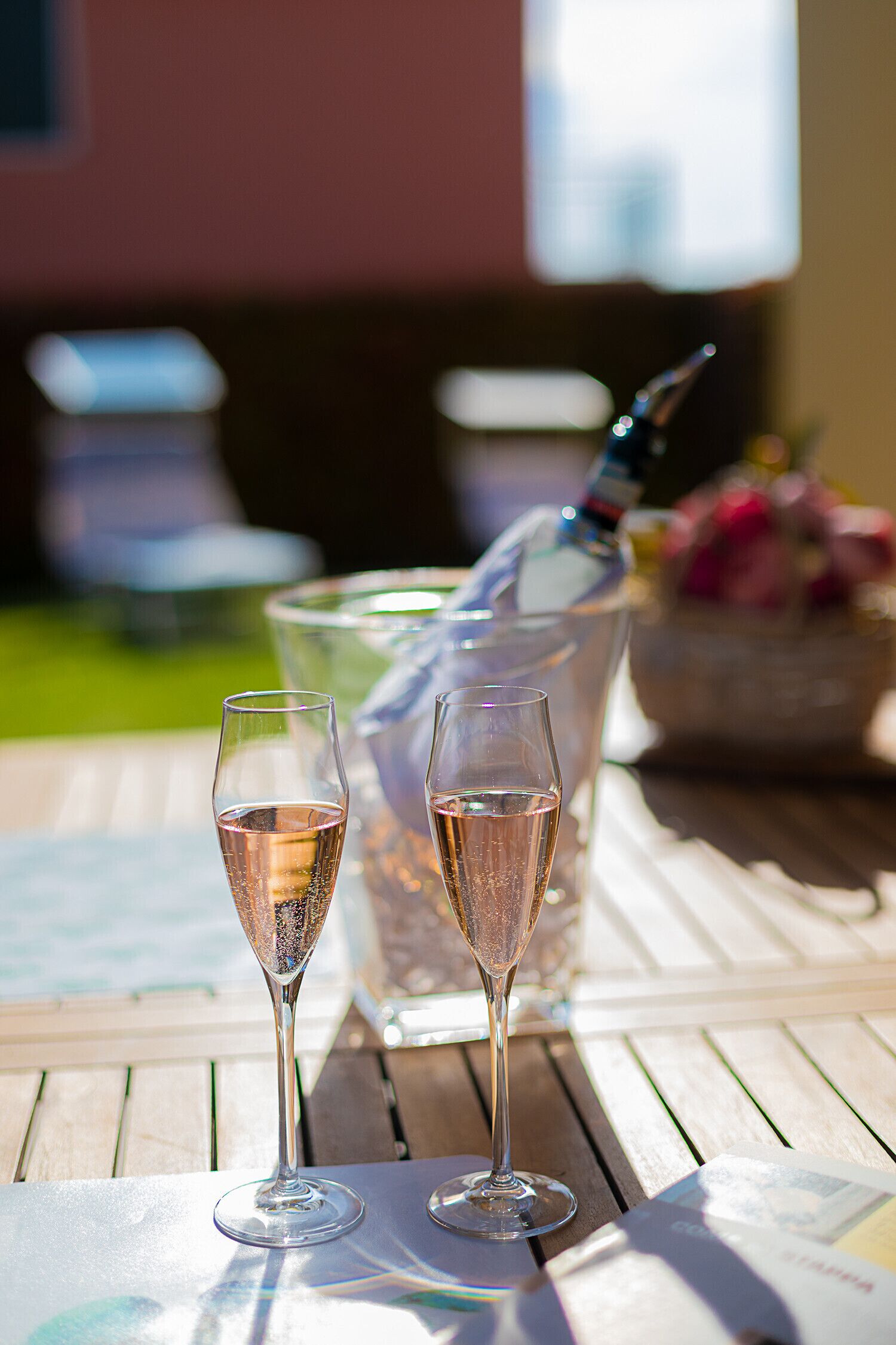 Two champagne flutes on a wooden table with a bottle of champagne and a glass pitcher in the background.