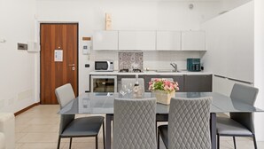 Et moderne køkken med hvide skabe, en mikrobølgeovn og en kaffemaskine. Der er et spisebord med fire stole og en vase med blomster.