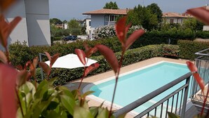 En swimmingpool omgivet af en have, hvid parasol og en bygning i baggrunden.