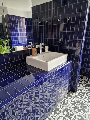 Een badkamer met een wit wastafelmeubel, zwart- en blauwe tegels en een vloer met een patroon.